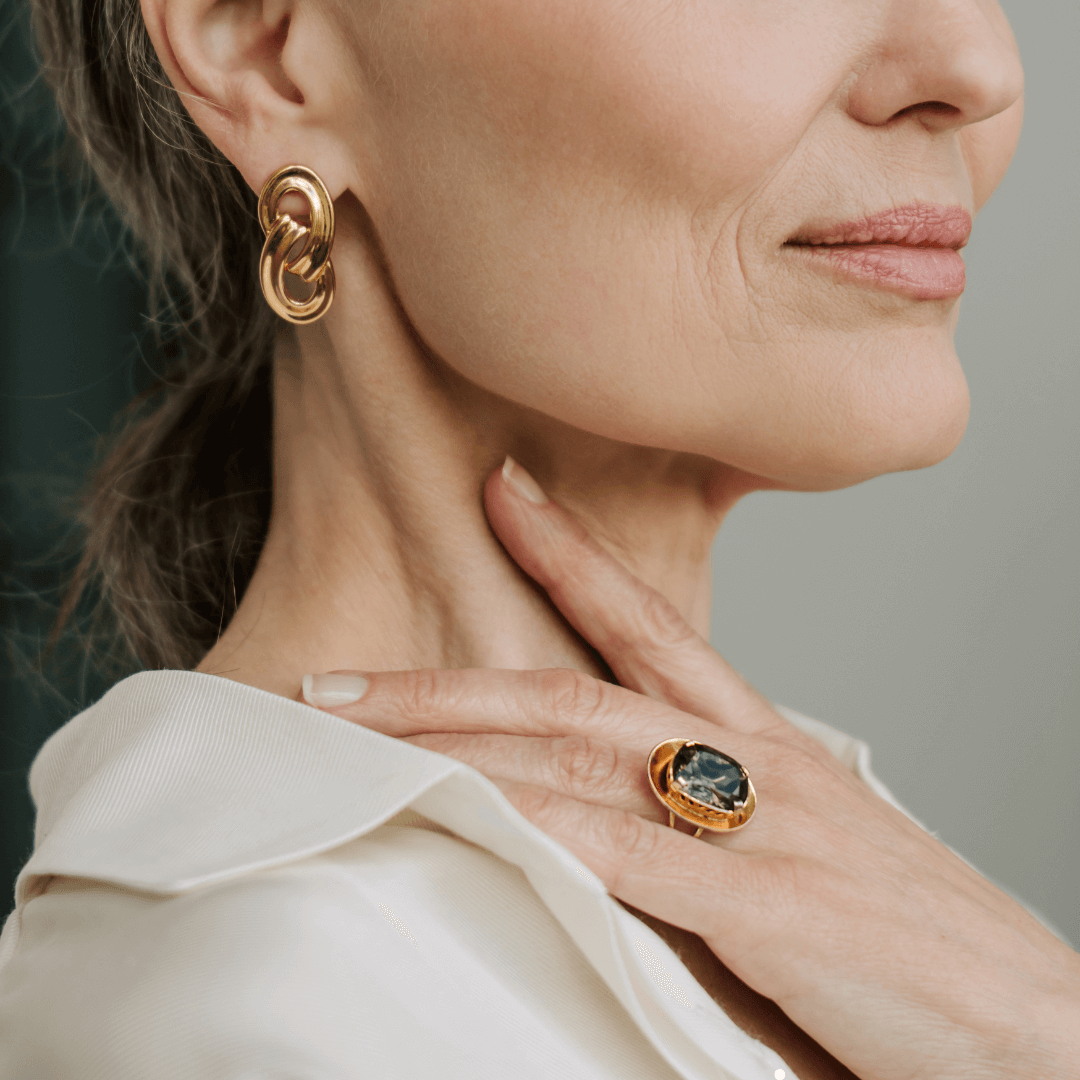 She's wearing a ring with what appears to be a dark-colored stone and hoop earrings. The overall style is minimalist and elegant.