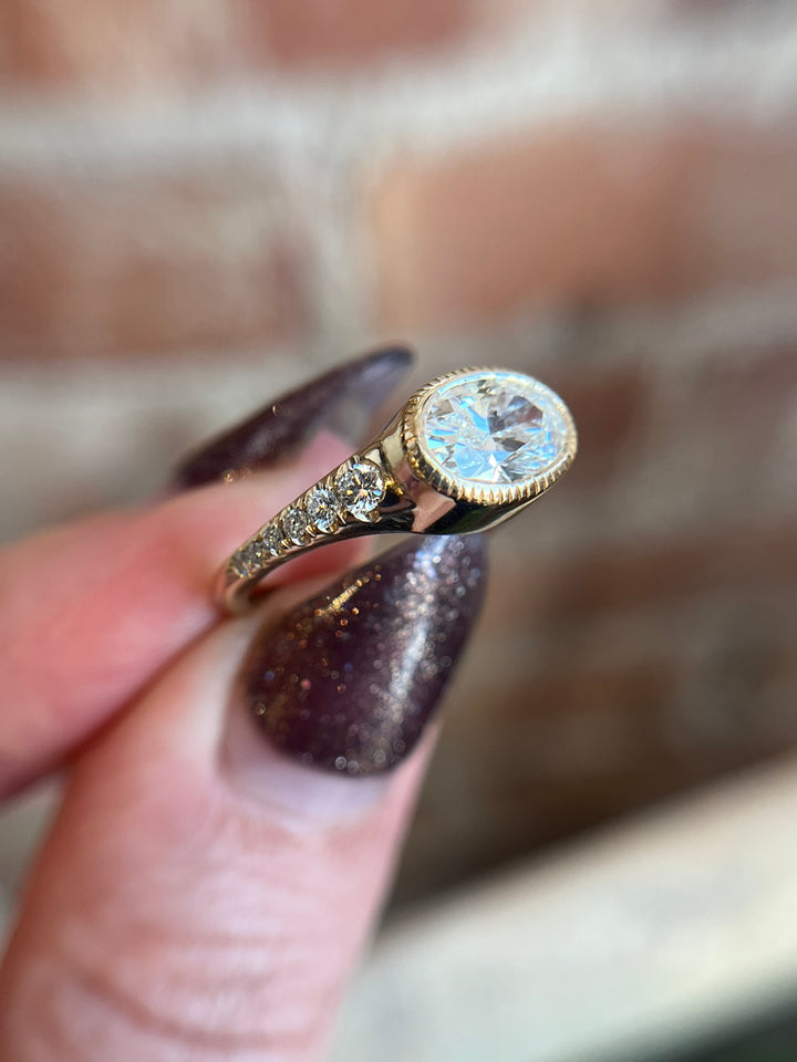 18K yellow gold oval diamond engagement ring with pavé side stones, worn on hand in lifestyle photo.