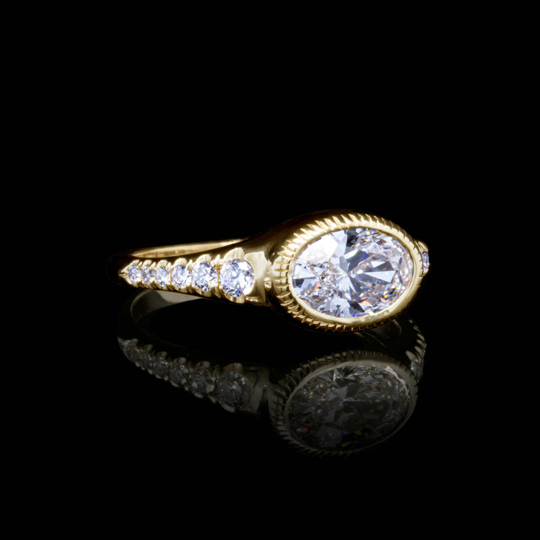 Yellow gold oval diamond ring with pavé diamonds, side angle on reflective black background.