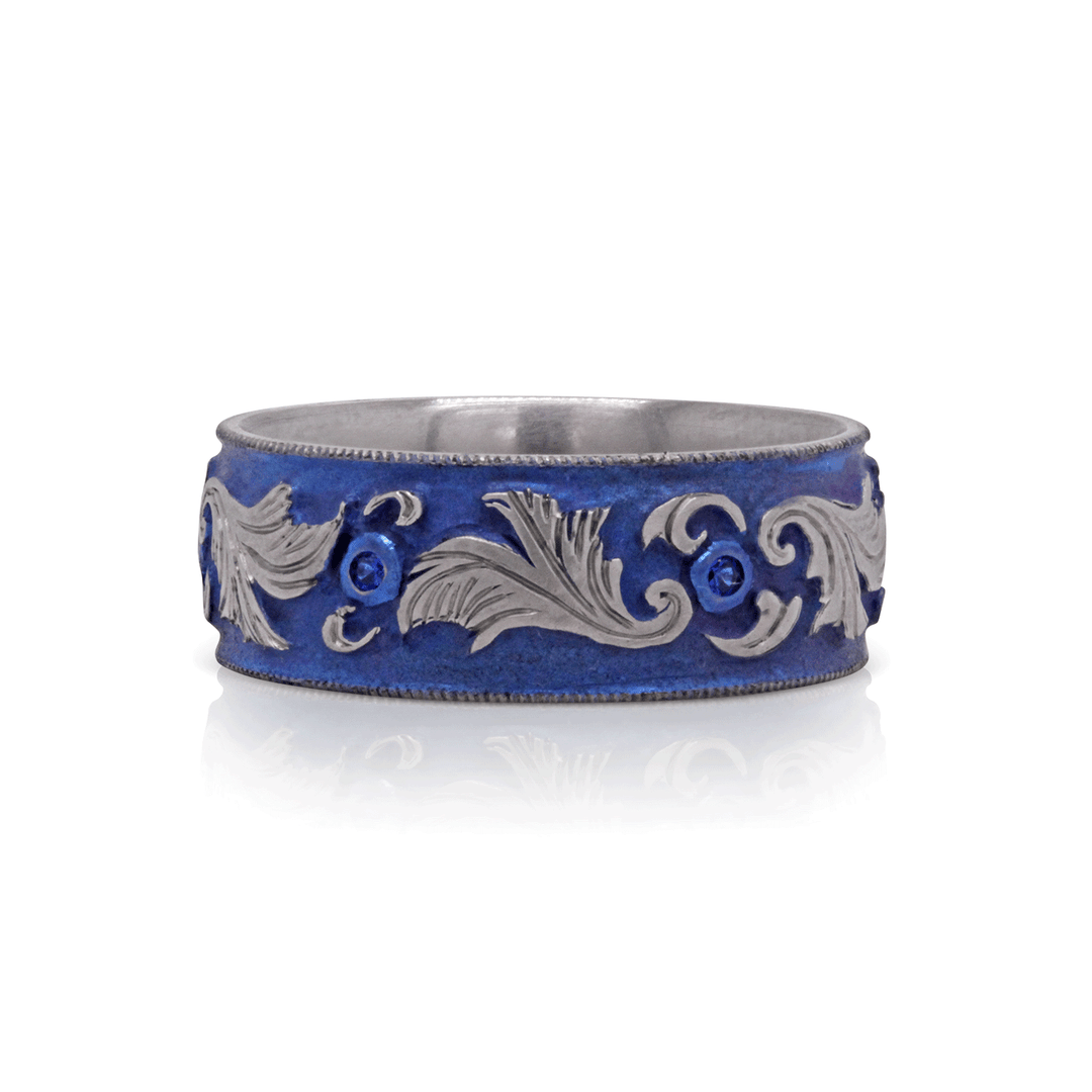 8mm titanium ring with blue anodized finish and intricate scrollwork, set with six 1mm lab-grown blue sapphires, size 9.25, displayed on a white background.