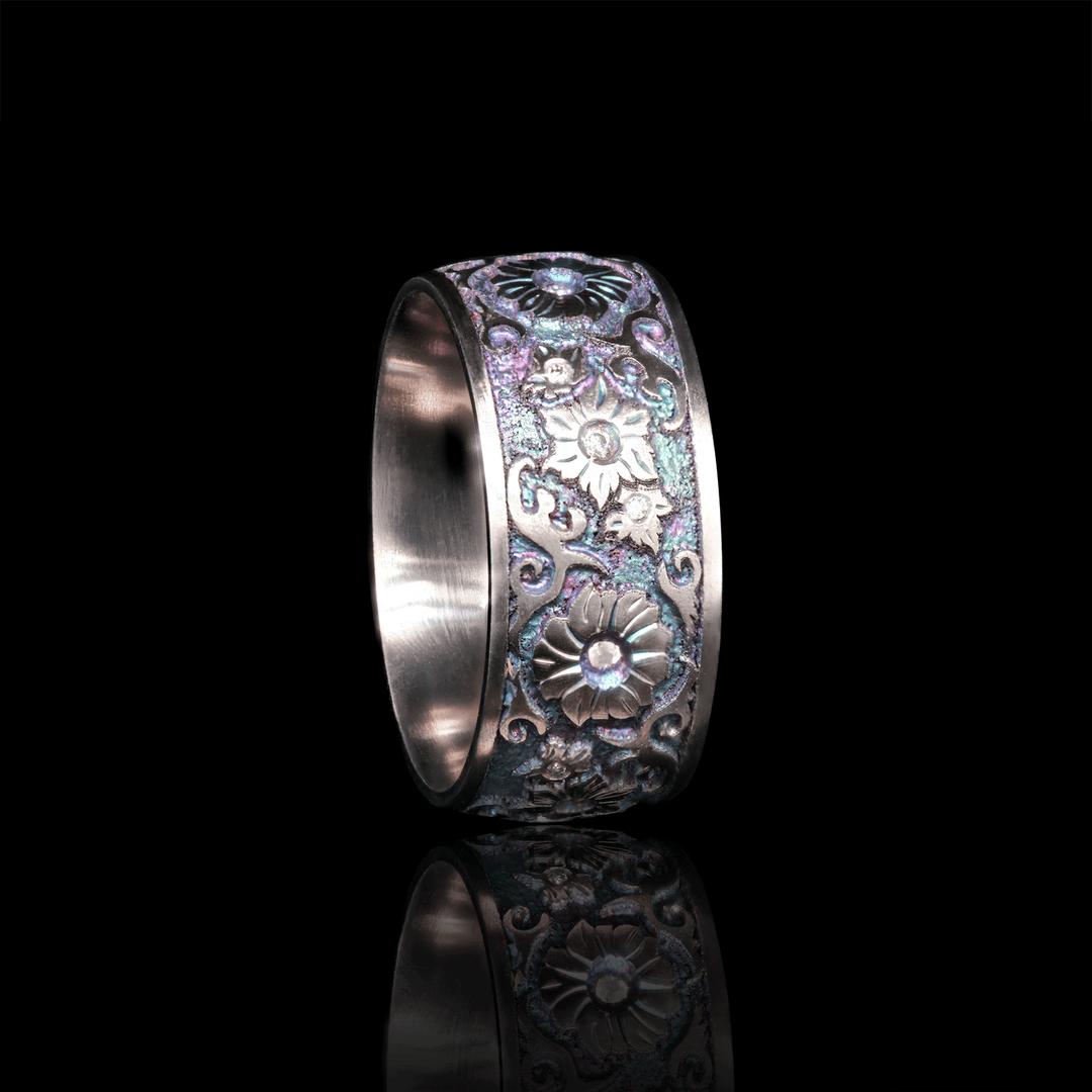 Side view of Floral Fantasy ring in titanium, showcasing floral engravings with white moissanite stones set in bezel, against a black background.
