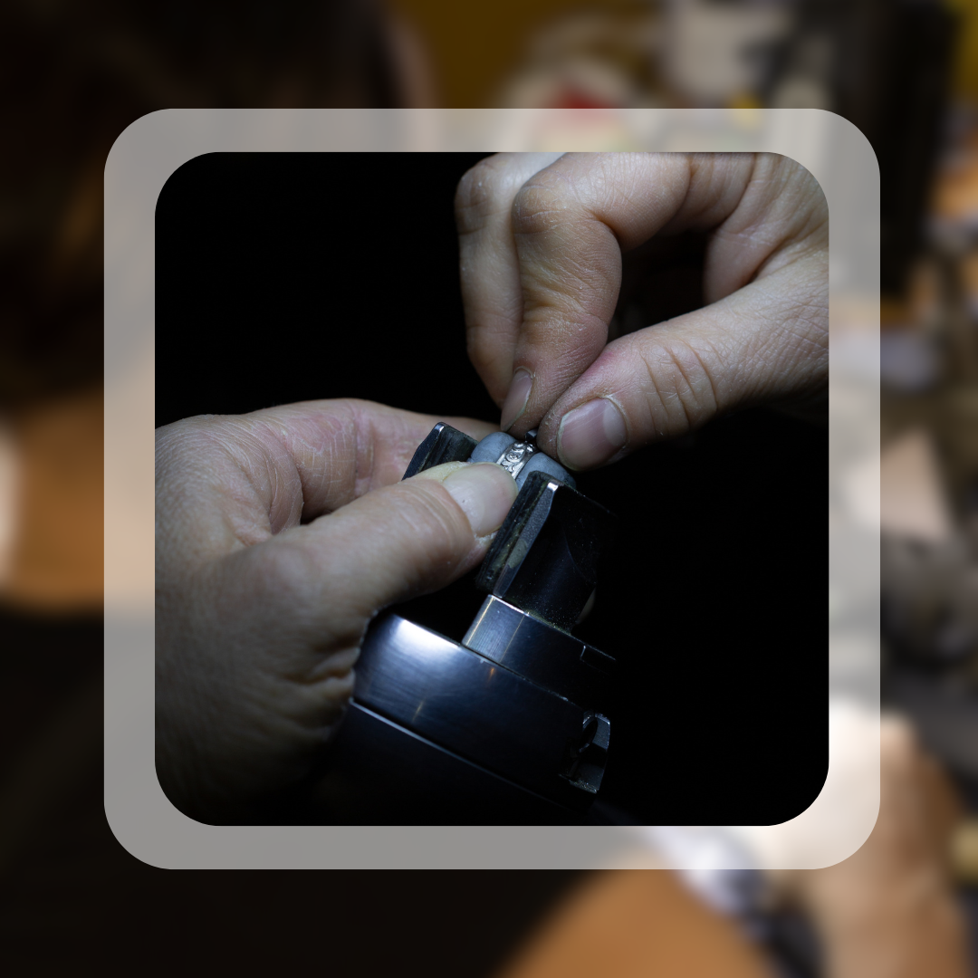 A close-up of hands meticulously working on a jewellery piece under a magnifying tool. The photo highlights craftsmanship and excellence