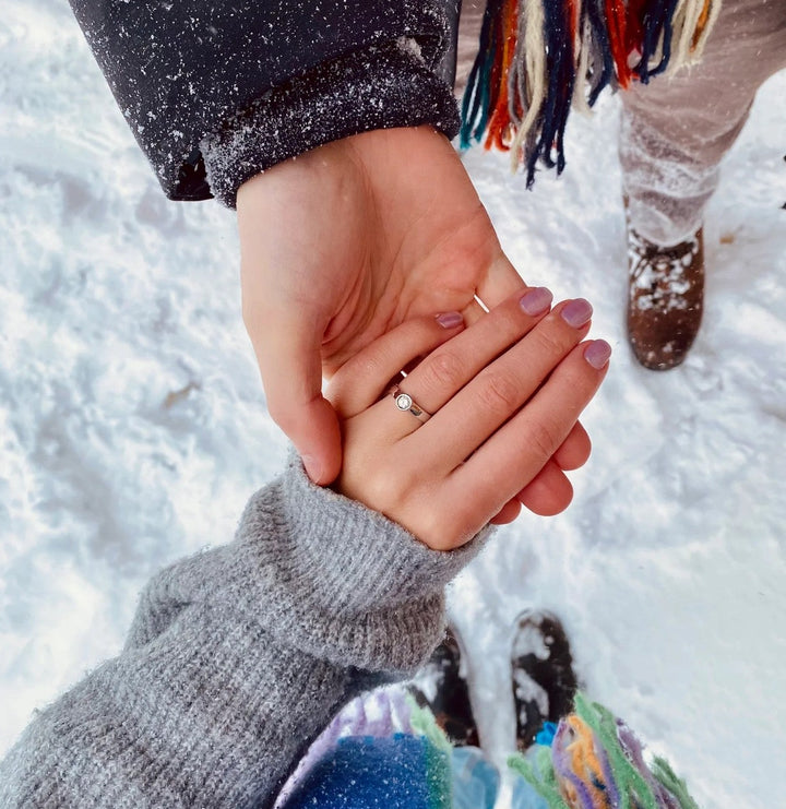 Two people holding hands in the snow, with one person wearing a colourful scarf. showing off their platinum custom engagement ring with heirloom diamond