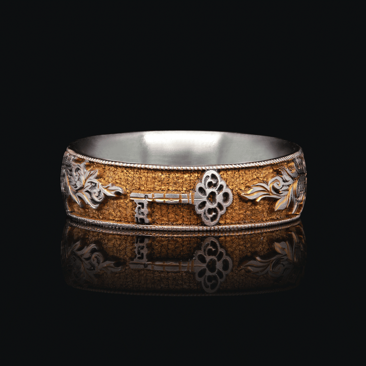 8mm wide titanium ring with gold anodized finish and intricate lock, key, and scroll engravings, highlighted against a black background, size 6.5