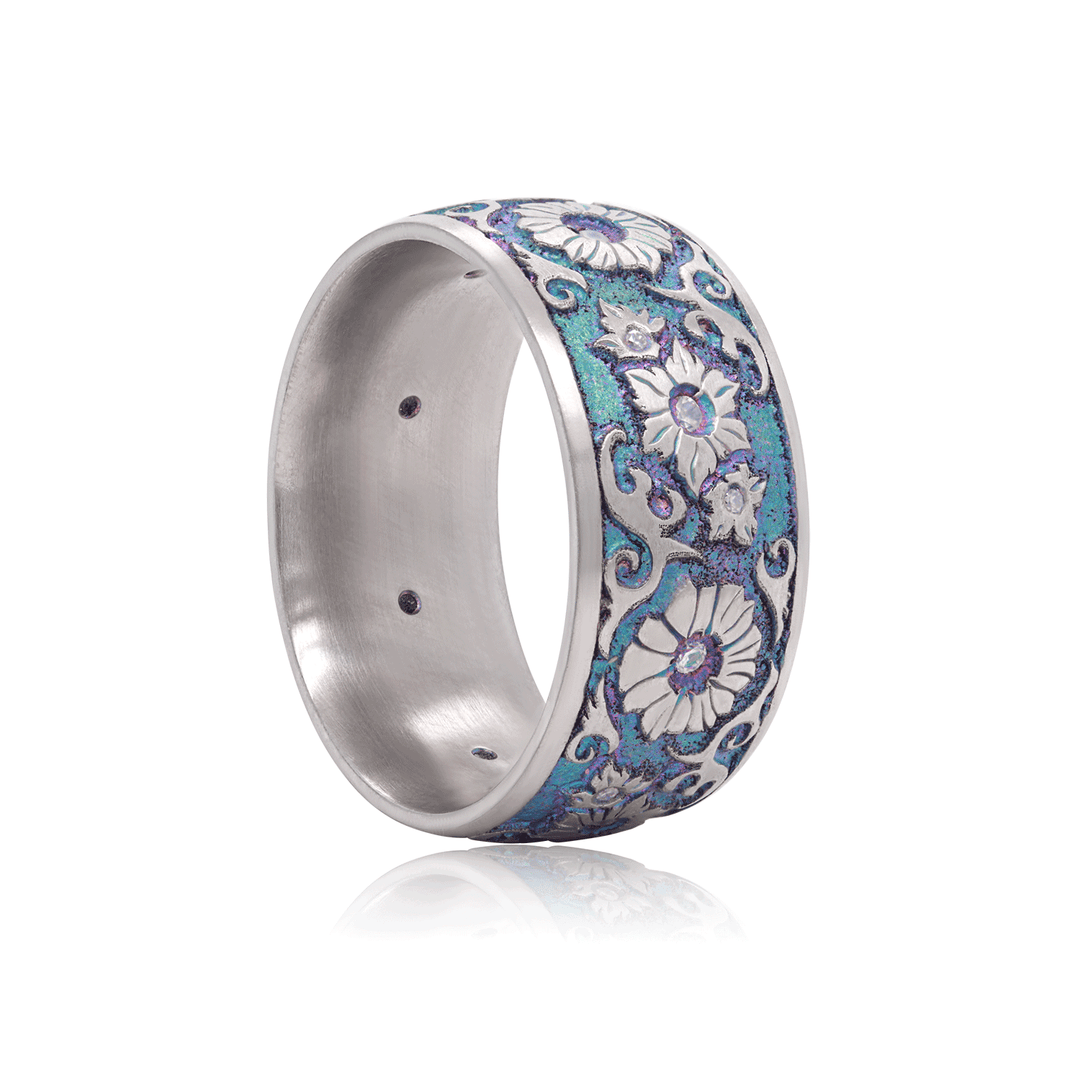 Angled view of titanium ring with iridescent finish and detailed floral design, highlighted by white moissanite stones, displayed against a white background.