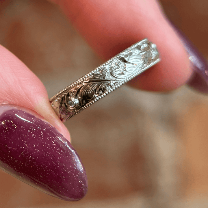 Close-up of a custom hand-engraved platinum wedding band with floral scrollwork, featuring delicate diamonds set along the band.