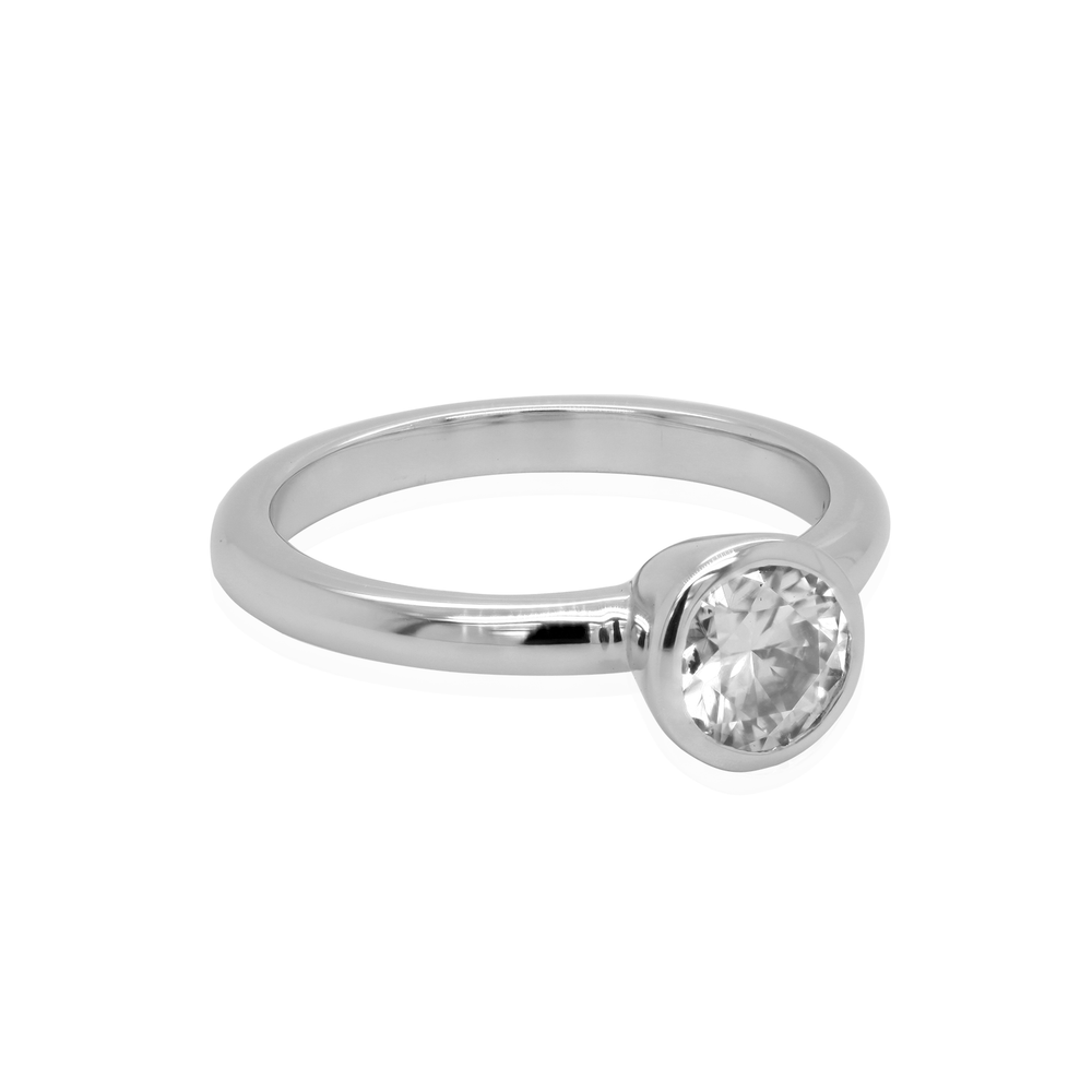Three quarter view of an 18K white gold solitaire ring. A brilliant moissanite gemstone is bezel-set in the center of the polished band.